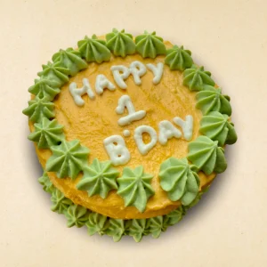Round dog birthday cake with yellow frosting and green star-shaped patterns