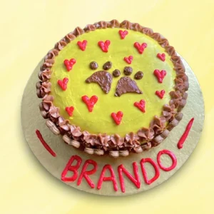 Yellow round dog cake with pink and brown cream hearts and paw print in the middle